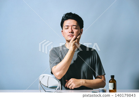 一位三十多歲的亞洲男子閉上眼睛，撫摸自己的臉，神情清新放鬆：這是植物和有機保養品的效果。 140179843