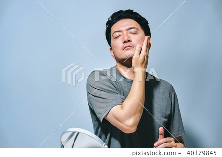 一位三十多歲的日本男子閉著眼睛，撫摸著自己的皮膚，感受它的狀況，看起來很放鬆。 （男士美容） 140179845