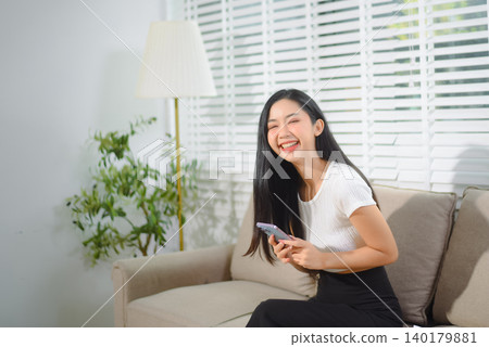 Asian businesswoman working from home on a cozy sofa, reviewing documents in a modern living room with a comfortable remote work lifestyle vibe. Asian businesswoman working from home on a cozy sofa, reviewing documents in a modern living room with a comfortable remote work lifestyle vibe. 140179881