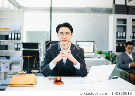 Confident Asian lawyer using tablet with gavel and justice scales on desk, looking at camera. Perfect for law, justice, business, and modern legal technology themes. Confident Asian lawyer using tablet with gavel and justice scales on desk, looking at camera. Perfect for law, justice, business, and modern legal technology themes. 140180018