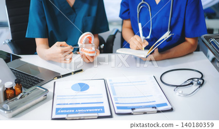 Two dentists in uniform type dental history on laptop with X-ray and tooth model on desk. Modern oral care, teamwork Two dentists in uniform type dental history on laptop with X-ray and tooth model on desk. Modern oral care, teamwork 140180359