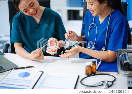 Two dentists in uniform type dental history on laptop with X-ray and tooth model on desk. Modern oral care, teamwork 140180364
