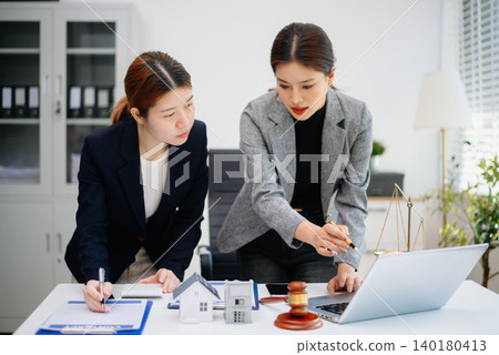 Real estate agent discussing property contract with client, showing house model, agreement, and legal consultation for home buying and investment. Real estate agent discussing property contract with client, showing house model, agreement, and legal consultation for home buying and investment. 140180413