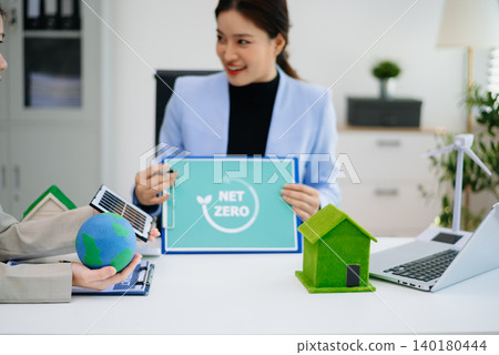 Businesswomen discussing renewable energy with solar panel and eco-friendly house model, focusing on sustainability, green power Businesswomen discussing renewable energy with solar panel and eco-friendly house model, focusing on sustainability, green power 140180444
