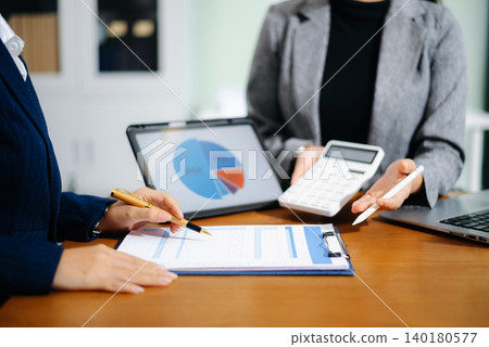 Two businesswomen review cash flow forecast and business growth charts on tablet and clipboard in office. Finance, data analytics, and planning concept for professionals. 140180577