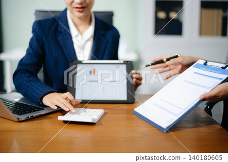 Two professional women in suits reviewing financial charts and analytics on paper and tablet in office. Business analysis, planning, and corporate strategy concept. Two professional women in suits reviewing financial charts and analytics on paper and tablet in office. Business analysis, planning, and corporate strategy concept. 140180605