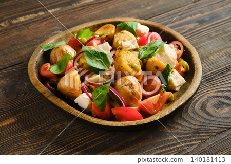Warm potato and feta salad with tomatoes and herbs served on a wooden plate Warm potato and feta salad with tomatoes and herbs served on a wooden plate 140181413