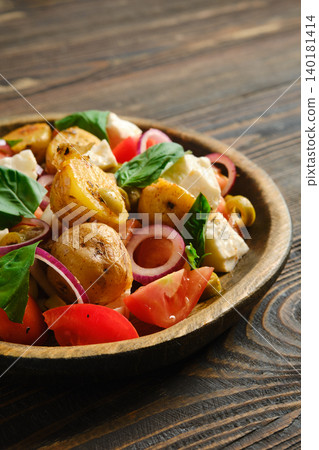 Warm potato and feta salad served on a wooden plate in a cozy kitchen setting Warm potato and feta salad served on a wooden plate in a cozy kitchen setting 140181414