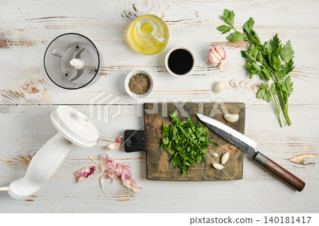 Preparing herbs and garlic on a wooden board with kitchen tools in a bright setting Preparing herbs and garlic on a wooden board with kitchen tools in a bright setting 140181417
