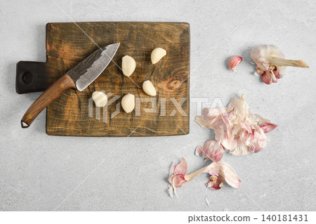 Garlic cloves and knife on wooden cutting board with garlic peels scattered around Garlic cloves and knife on wooden cutting board with garlic peels scattered around 140181431