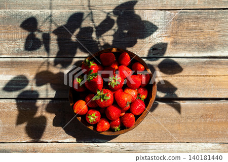 Fresh strawberries in brown bowl on wooden table with shadows from leaves in afternoon light Fresh strawberries in brown bowl on wooden table with shadows from leaves in afternoon light 140181440