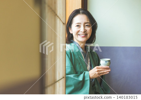 A woman in a yukata drinking tea at a ryokan (Japanese inn). A woman in a yukata drinking tea at a ryokan (Japanese inn). 140183015