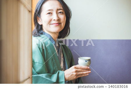 A woman in a yukata drinking tea at a ryokan (Japanese inn). A woman in a yukata drinking tea at a ryokan (Japanese inn). 140183016