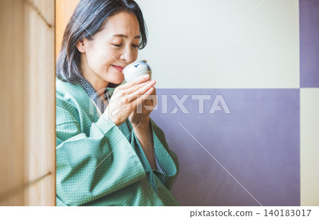 A woman in a yukata drinking tea at a ryokan (Japanese inn). A woman in a yukata drinking tea at a ryokan (Japanese inn). 140183017