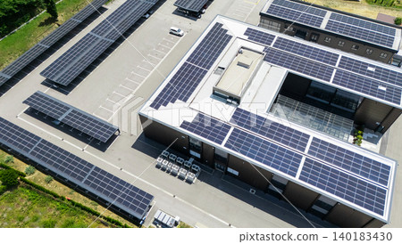 Aerial view of building with solar panels on a roof and parking space with solar canopies. 140183430