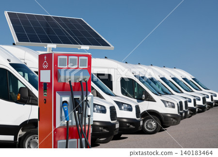 Electric vans are charging from electric vehicle charging stations with built-in solar panels on a city street.. Electric vans are charging from electric vehicle charging stations with built-in solar panels on a city street.. 140183464
