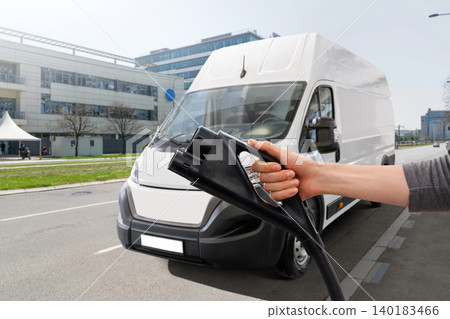 Hand with charging plug on a background of electric van Hand with charging plug on a background of electric van 140183466