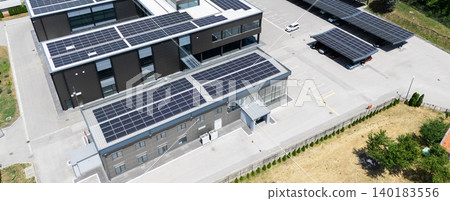 Aerial view of building with solar panels on a roof and parking space with solar canopies. Aerial view of building with solar panels on a roof and parking space with solar canopies. 140183556
