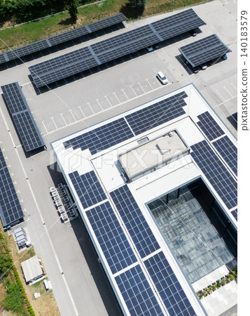 Aerial view of building with solar panels on a roof and parking space with solar canopies. Aerial view of building with solar panels on a roof and parking space with solar canopies. 140183579