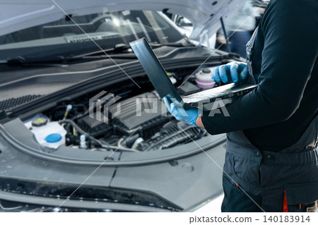 Serviceman with laptop checks car software in car service. Serviceman with laptop checks car software in car service. 140183914
