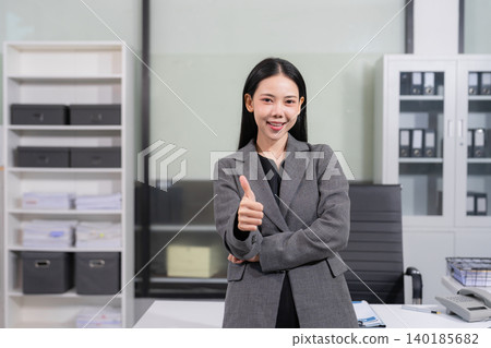 Happy Asian Businesswoman showing thumbs up gesture for success and approval in modern office. Happy Asian Businesswoman showing thumbs up gesture for success and approval in modern office. 140185682