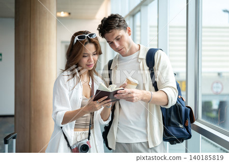 Asian woman girlfriend showing passport to white man boyfriend going on a trip standing in airport. Asian woman girlfriend showing passport to white man boyfriend going on a trip standing in airport. 140185819