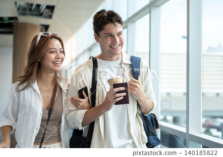 Happy asian woman girlfriend linking arms with white man boyfriend while walking in the airport. Happy asian woman girlfriend linking arms with white man boyfriend while walking in the airport. 140185822
