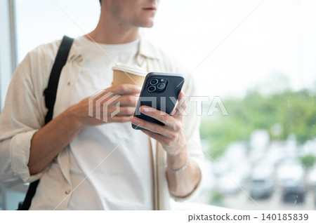 Close up of white caucasian man tourist holding coffee and smartphone looking outside the glass wall Close up of white caucasian man tourist holding coffee and smartphone looking outside the glass wall 140185839