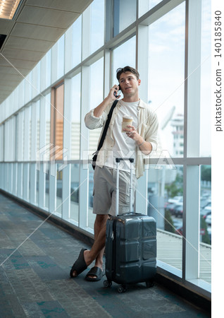 White caucasian man tourist hold coffee talking on phone standing beside luggage waiting in airport. 140185840