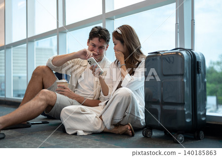 Asian woman girlfriend laughing at phone with white man boyfriend an luggage sits on airport's floor Asian woman girlfriend laughing at phone with white man boyfriend an luggage sits on airport's floor 140185863