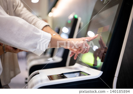 Close up of a woman tourist's hands doing self check in touching screen on kiosk machine in airport. Close up of a woman tourist's hands doing self check in touching screen on kiosk machine in airport. 140185894