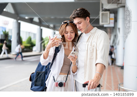 Asian woman girlfriend and white man boyfriend looking at phone checking map as standing in airport. Asian woman girlfriend and white man boyfriend looking at phone checking map as standing in airport. 140185899
