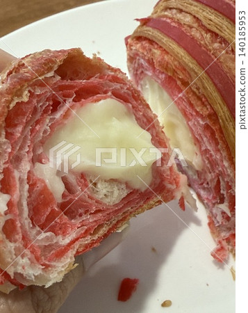 Strawberry-flavored croissant with a creamy filling, partially sliced, showing texture and layers 140185953