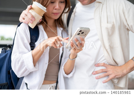 Close up of woman girlfriend looking at phone beside a boyfriend while standing waiting in airport. Close up of woman girlfriend looking at phone beside a boyfriend while standing waiting in airport. 140185981