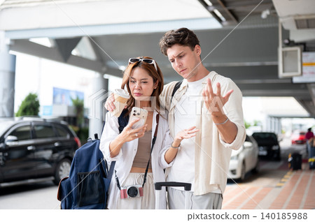 Confused asian woman girlfriend and white man boyfriend looking at phone while standing in airport. Confused asian woman girlfriend and white man boyfriend looking at phone while standing in airport. 140185988