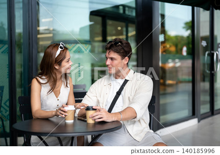 Asian woman girlfriend talking touching white man boyfriend's hand sitting at table in coffee shop Asian woman girlfriend talking touching white man boyfriend's hand sitting at table in coffee shop 140185996
