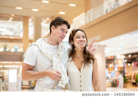 White man boyfriend pointing and asian woman girlfriend looking as shopping together in luxury mall. White man boyfriend pointing and asian woman girlfriend looking as shopping together in luxury mall. 140186004