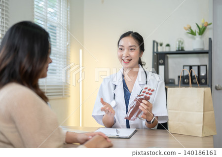 Happy asian woman doctor showing medicine explaining talking to patient at table in hospital clinic. Happy asian woman doctor showing medicine explaining talking to patient at table in hospital clinic. 140186161