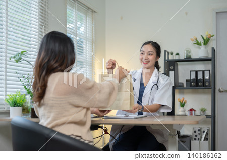 Pretty asian woman doctor giving medicine prescription to young patient at table in hospital clinic. Pretty asian woman doctor giving medicine prescription to young patient at table in hospital clinic. 140186162