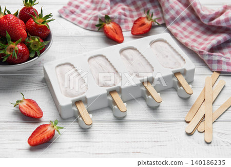 Strawberry popsicles in making process on white wooden surface Strawberry popsicles in making process on white wooden surface 140186235