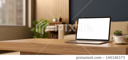 White screen laptop with coffee cup and books on wooden table across sofa and window in living room. White screen laptop with coffee cup and books on wooden table across sofa and window in living room. 140186373
