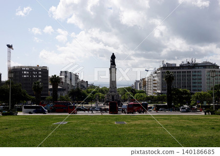 City square with a large stone monument and traffic under a bright cloudy sky 140186685