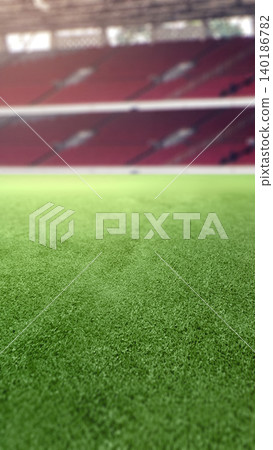 A low-angle, selective focus view of green turf grass in an empty sports stadium with blurred red spectator seats A low-angle, selective focus view of green turf grass in an empty sports stadium with blurred red spectator seats 140186782