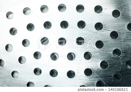 Macro shot of a shiny silver metallic colander surface with circular perforated holes and scratch details, creating a clean industrial pattern Macro shot of a shiny silver metallic colander surface with circular perforated holes and scratch details, creating a clean industrial pattern 140186821