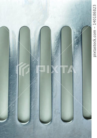 Macro view of a clean brushed metal surface with vertical slotted openings, showing details of industrial design, ventilation grates, or drainage filters Macro view of a clean brushed metal surface with vertical slotted openings, showing details of industrial design, ventilation grates, or drainage filters 140186823