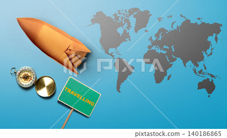 A creative flat lay representation of world travel featuring an orange paper rocket, a golden compass, and a green "TRAVELLING" sign on a blue background with a grey world map A creative flat lay representation of world travel featuring an orange paper rocket, a golden compass, and a green "TRAVELLING" sign on a blue background with a grey world map 140186865
