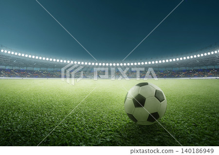 A classic black and white soccer or football ball rests on a lush green grass field under the brilliant floodlights of a large, professional stadium during a night sports event A classic black and white soccer or football ball rests on a lush green grass field under the brilliant floodlights of a large, professional stadium during a night sports event 140186949