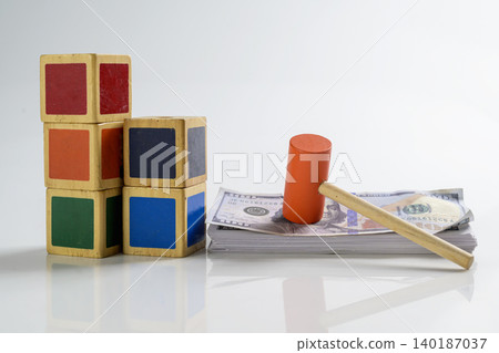 A toy orange wooden gavel on a stack of US hundred-dollar bills next to colorful building blocks, representing child custody costs, education savings, or family court A toy orange wooden gavel on a stack of US hundred-dollar bills next to colorful building blocks, representing child custody costs, education savings, or family court 140187037
