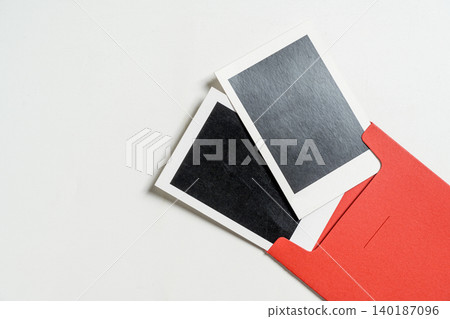 Minimalist top-down view of two blank instant photo frames coming out of a vibrant red envelope, placed on a clean white textured surface. Ideal for memory or message concepts Minimalist top-down view of two blank instant photo frames coming out of a vibrant red envelope, placed on a clean white textured surface. Ideal for memory or message concepts 140187096