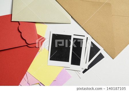 A variety of colorful envelopes, including red and kraft brown, scattered with small yellow and pink note cards and black labels on a white background, perfect for crafting or mail themes 140187105